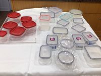 Full view of food storage containers with assorted colored lids arranged on a white cloth surface, showing variety of shapes and sizes.