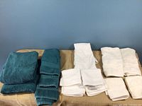 Photo showing six white towels and two jade green towels folded and laid out on a table with a blue wall background.