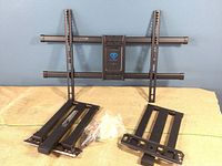 Wide shot of black Perlesmith TV wall mount with metal arms and mounting hardware laid out on a cloth surface
