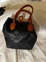 Black purse with brown handles, perforated diamond pattern and magnetic strap shown upright