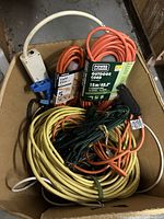 Box containing multiple extension cords in various colors, some with product labels.