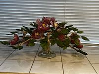 Front view of glass sculpture centerpiece with pink flowers and green leaves on a clear glass base.