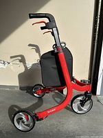 Side view of red "Nitro" 3-wheel rollator with black hand grips, brake lever, and black shoppers bag.
