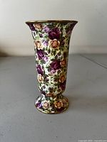 Photo showing full front exterior of the vase with dense rose floral pattern and gold trim at rim and base.