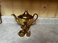 Front and side views of the full set showing large gold reflective teapot and miniature tea set including small teapot, sugar bowl, and creamer with wear visible.