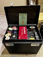 Black hard carrying case open, showing accessories tray with tin, oil can, thread and bobbins