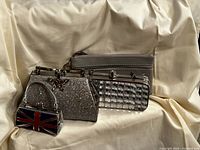 Four purses including silver glitter clutch with butterfly clasp, rectangular silver glitter clutch with chain, grey change purse, and Union Jack mini handbag, arranged on cream fabric.