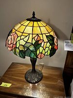 Front view of lamp lit showing rose and leaf stained glass shade and base