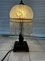 Full view of the lamp lit showing frosted glass shade with swirl pattern and hanging beaded fringe.