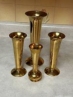 Four gold-tone vintage Royal Winton bud vases arranged together, showing relative sizes and shapes.
