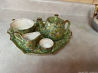 Front view of tray holding teapot, cup, creamer, sugar bowl and lid