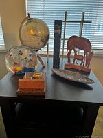 Murano glass fish aquarium paperweight, globe with wooden stand, wooden Momma Wolf with cub figurine, Haida Beaver tray and a wooden box on black table near window.