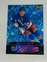 Front side of Alexis Lafreniere hockey card with blue dazzler holographic pattern, player in Rangers jersey skating with stick.