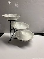 Front view of the three-tiered stand with scalloped white porcelain plates on a black metal frame.