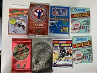 Photo of 8 unopened packs of sports trading cards including hockey, football, and baseball from the brands Score, National Hockey Card Day, NFL Pro Set, Donruss, and Premier O-Pee-Chee.