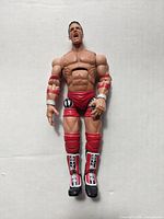 Front view of the AJ Styles action figure showing red wristbands, elbow pads, trunks, knee pads and boots with detailed sculpting and facial expression.