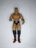 Front view of the articulated wrestling action figure showing muscular physique, facial details, black trunks, and red/black boots.