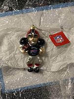 Front view of Buffalo Bills football player Christmas ornament with NFL tag and attached gold hanging loop on bubble wrap background.