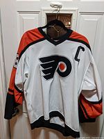 Full front view of white, orange and black Philadelphia Flyers jersey with captain C and Flyers logo