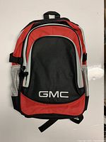 Front view of GMC backpack showing red, black, gray colors and GMC logo embroidered on front pocket.