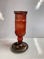 Photo of a red glass hummingbird feeder with a ribbed top, floral embossing on glass, and a metal base with floral feeding ports.
