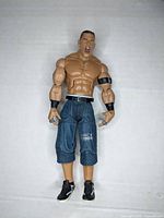 Front view of the John Cena action figure showing muscular upper body and denim-style shorts.