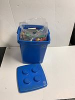 Blue plastic LEGO-brick-shaped storage bin with lid, containing LEGO pieces.