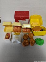 Overview of vintage plastic McDonald's food toys with red storage container, yellow containers, brown hamburgers, fries, lettuce, and BBQ sauce toy pieces