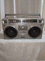 Front view of silver boombox showing dual speakers, cassette deck, tuning scale and controls