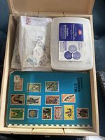 Contents of the lot showing a blue stamp album, a cleaning cloth container, and resealable bags with loose stamps.