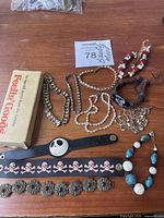 Mixed vintage bracelets laid on wooden surface including Feelin' Goods wooden bead bracelet in box, chain link bracelets, faux pearls, and novelty leather bands with skull designs.