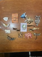 Collection of 14 vintage animal and insect brooches on wooden surface, showing variety of styles and finishes.