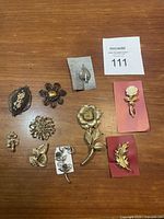 Top view showing all 10 vintage metal floral brooches arranged on a wooden surface.