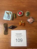 Eight vintage brooches arranged on wooden surface, including stones of multiple colors and shapes with metal detailed settings.