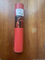 Red cylindrical tube containing the rolled uncut press sheet, showing seller's lot label with price and barcode.