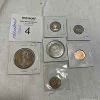Seven assorted international coins carded individually in cardboard holders and one plastic sleeve, showing front sides with country and date labels, price tags written on the holders.