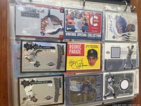 Photo of baseball cards in plastic sleeves inside binder showing player action shots, memorabilia pieces, signatures, and rookie cards.