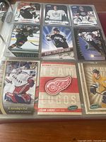Photo of hockey cards with various players including goalies and skaters from different NHL teams, showing front of individual cards in protective sleeves inside binder