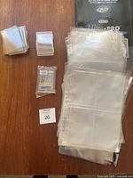 Clear plastic card sleeves, top loaders, and multiple Ultra PRO binder pages for sports cards on wood surface.