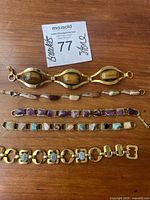 Five vintage bracelets laid flat on a wooden surface showing various stone types and gold-toned metal links.