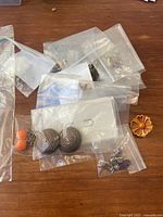 Lot of various vintage clip on earrings in ziplock bags on wood surface, includes spiral, floral, and assorted shapes and colors.