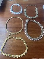 Top-down photo showing 5 vintage necklaces on wooden surface, variety of bead and chain styles