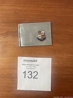 Front view of vintage metal stamp holder on wood surface with embossed 'Stamps' and a colorful crest emblem