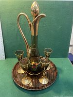 Front view of the vintage liquor decanter with five matching glasses on a round tin tray with woodgrain pattern.