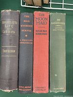 Four vintage books standing upright showing spines: Macaulay Life and Letters, The Man Without Nerves, The Moon Maid, The Masquerader