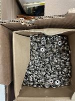 Open cardboard box filled with numerous silver metal snap fasteners.