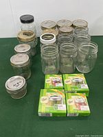 Multiple clear glass canning jars, some with lids, shown with four unopened boxes of Ball brand lid inserts in green packaging.
