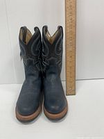 Front view of both roper cowboy boots with a ruler for height reference, showing blue and black leather with decorative stitching and natural wood tone heel.