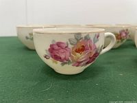 Close-up side view of one teacup showing detailed rose floral pattern in pink and yellow hues.