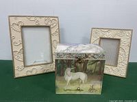 Unicorn music box with painted forest scene, two carved picture frames in cream color beside it